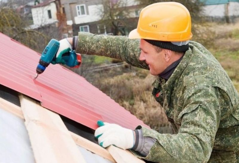 Монтажник устанавливает профнастил на крышу